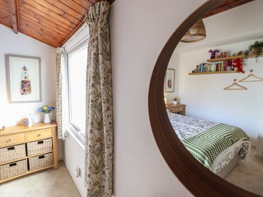 A bedroom with a wooden dresser with baskets flowers on it and a bed with patterned bedding as seen in a round mirror at Branwen in Porthmadog