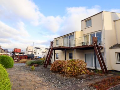 An exterior view of a two-story building with balconies and stairs and a gravel garden with shrubs at Branwen in Porthmadog