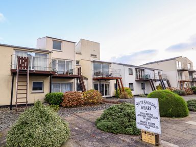 A row of residential buildings with balconies and staircases with bushes and a sign in front at South Snowdon Wharf in Porthmadog