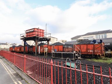A railway yard with coal-filled red rail cars and a water tower at Festiniog Railway in Porthmadog