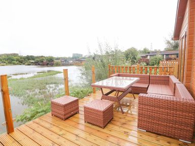 A wooden deck with wicker patio furniture overlooking a lake at Lakeside 12 in Carnforth