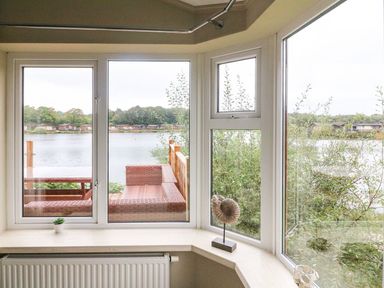 A window view overlooking a lake with outdoor seating and greenery at Lakeside 12 in Carnforth