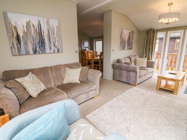 A living room with two brown sofas a light blue armchair a wooden coffee table and a dining area with wooden chairs at Lakeside 12 in Carnforth