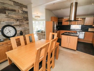 A dining area with wooden table and chairs next to a kitchen with wooden cabinets and stainless steel appliances at Lakeside 12 in Carnforth