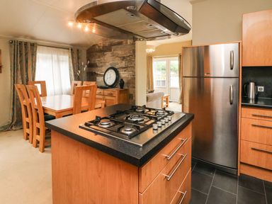 A kitchen with a gas stove island and wooden cabinets next to a dining area with a wooden table and chairs at Lakeside 12 in Carnforth