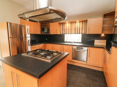 A kitchen with wooden cabinets a black countertop gas stove dishwasher and stainless steel refrigerator at Lakeside 12 in Carnforth