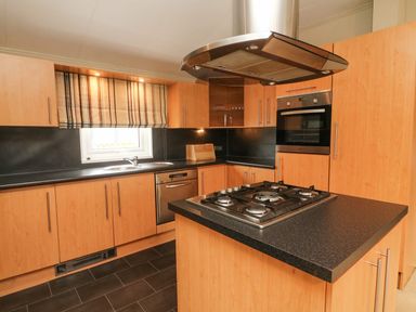 A kitchen with wooden cabinets a gas stove on an island and a window with a striped blind at Lakeside 12 in Carnforth