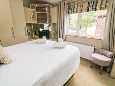 A bedroom with a white bed and rolled towels a window with striped blinds and a small upholstered chair at Lakeside 12 in Carnforth