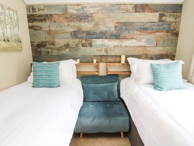 A bedroom with two single beds white bedding and blue pillows a blue cushioned chair between beds and a wooden paneled wall at Lakeside 12 in Carnforth