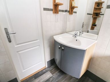 A bathroom sink with a mirror above and shelves beside a white door at Lakeside 12 in Carnforth