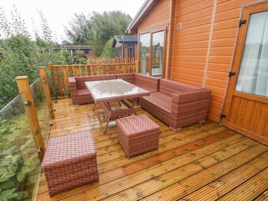 An outdoor wooden deck with brown wicker furniture including a corner sofa table and two stools at Lakeside 12 in Carnforth