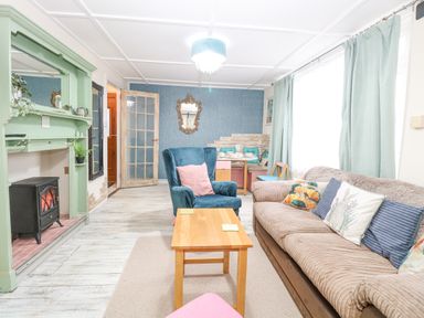 A living room with a beige sofa and blue armchair next to a wooden coffee table and green fireplace at White Rabbit Cross Lane in Eccles On Sea