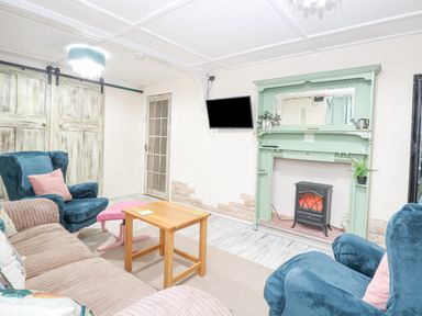 A sitting room with blue armchairs a beige sofa a wooden coffee table a green fireplace mantel and a wall-mounted television at White Rabbit Cross Lane in Eccles-On-Sea