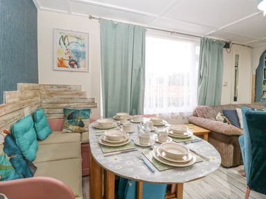 A dining area with a table set for six and a cushioned bench next to a window with curtains at White Rabbit Cross Lane in Eccles On Sea