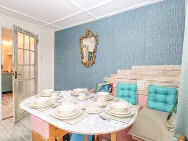 A dining area with a set table including plates cups and cutlery a bench with cushions and an ornate mirror on a blue textured wall at White Rabbit Cross Lane in Eccles-On-Sea