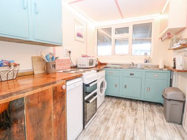 A kitchen with wooden countertops blue cabinets a stove dishwasher washing machine microwave and a window at White Rabbit Cross Lane in Eccles-On-Sea