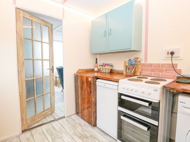 A kitchen with a wooden floor wooden countertops blue wall cabinets an electric stove dishwasher and a door leading to another room at White Rabbit Cross Lane in Eccles On Sea