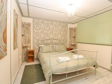 A bedroom with a double metal bed with green bedding two rolled towels two wooden bedside tables floral wallpaper and two abstract paintings at White Rabbit Cross Lane Eccles-On-Sea