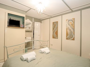 A bedroom with a bed with rolled towels a small TV mounted on the wall and two abstract paintings at White Rabbit Cross Lane in Eccles-On-Sea