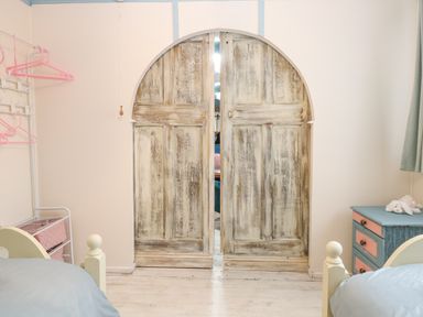 A bedroom with two beds a blue and pink chest of drawers and wooden arched double doors at White Rabbit Cross Lane in Eccles-On-Sea