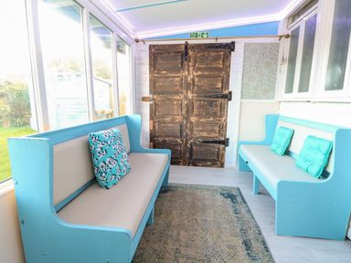 A seating area with two blue benches and cushions on a rug near wooden doors at White Rabbit Cross Lane Eccles On Sea