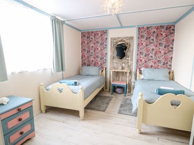 A bedroom with two single beds a blue and pink chest of drawers and a decorative mirror at White Rabbit Cross Lane in Eccles-On-Sea