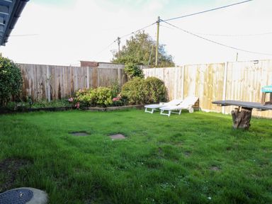 A backyard garden with green grass two white lounge chairs wooden fence and shrubs at White Rabbit Cross Lane in Eccles-On-Sea