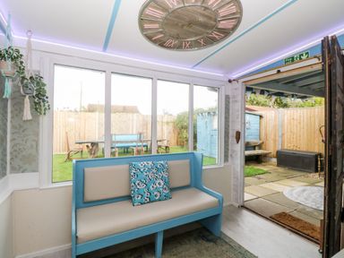 A sunroom with a blue bench and pillow looking out onto a garden with wooden furniture at White Rabbit Cross Lane Eccles-On-Sea