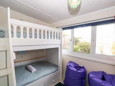 A bedroom with a white bunk bed a rolled towel on the bottom bed and two purple bean bags near a window at White Rabbit Cross Lane Eccles-On-Sea