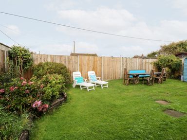 A garden with two white lounge chairs and wooden table with chairs on grass at White Rabbit Cross Lane in Eccles-On-Sea