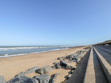 A sandy beach with large rocks and concrete steps along the shore at White Rabbit Cross Lane in Eccles-On-Sea