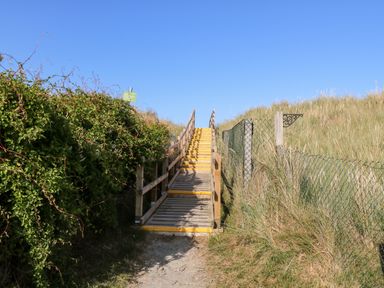 A wooden staircase with yellow edges leading up between grassy dunes and fences at White Rabbit in Eccles-On-Sea