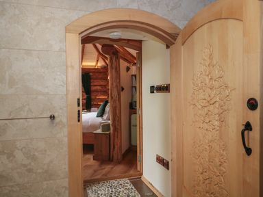 An open wooden door with carved floral designs leading to a bedroom with a bed and wooden beams at Copper Lodge in Chulmleigh