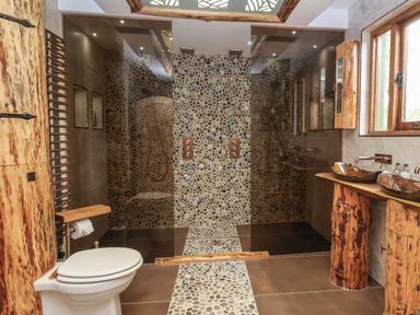 A bathroom with a stone tiled shower area two brown stone sinks on wooden pedestal counters a toilet and wooden accents at Copper Lodge in Chulmleigh