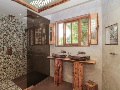 A bathroom with a pebble stone shower area wooden double sink counter and a window at Copper Lodge in Chulmleigh