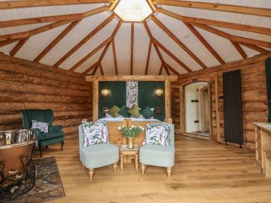 A bedroom with a wooden ceiling and walls two armchairs a wooden bed and an armchair at Copper Lodge in Chulmleigh