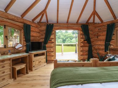 A bedroom with wooden furniture and green curtains in a log cabin at Copper Lodge in Chulmleigh