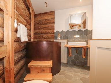 A bathroom with a copper bathtub wooden steps sink with a mirror and hexagonal tiles at Copper Lodge in Chulmleigh