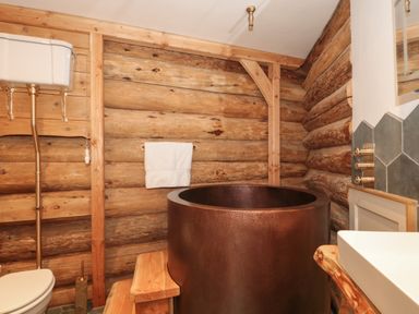 A bathroom with a copper tub wooden walls and a white toilet at Copper Lodge in Chulmleigh