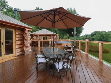 An outdoor wooden deck with a metal table and chairs under a large umbrella at Copper Lodge in Chulmleigh