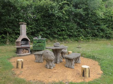 An outdoor patio area with a stone table and benches near a wood-fired oven and planter at Copper Lodge in Chulmleigh