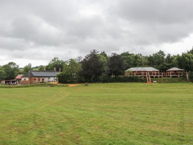 A large grassy field with a dirt path leading to buildings and trees in the background at Copper Lodge in Chulmleigh