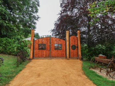 A wooden gate with two main doors and a smaller door next to it along a dirt driveway at Copper Lodge in Chulmleigh