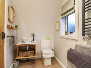 A bathroom with a white toilet wooden sink cabinet round mirror and window at Yes Deer in Ashbourne