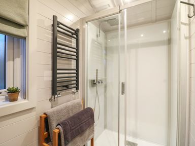 A bathroom with a glass shower enclosure a black towel radiator and towels at Yes Deer in Ashbourne