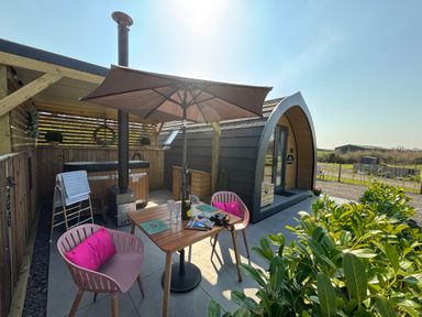 An outdoor seating area with a table umbrella chairs and a wooden cabin at Yes Deer in Ashbourne