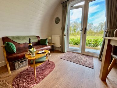 A living room with a sofa and coffee table next to glass doors showing an outdoor view at Yes Deer in Ashbourne
