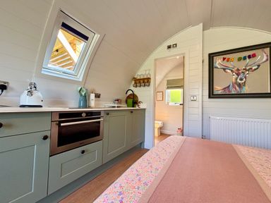A bedroom with a bed and an adjacent kitchenette with a window and a door leading to a bathroom at Yes Deer in Ashbourne