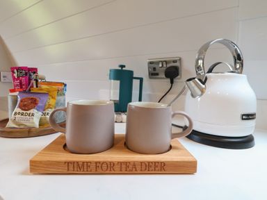 Two mugs on a wooden tray with time for tea deer engraved beside a white kettle and packets of biscuits on a tray at Yes Deer in Ashbourne