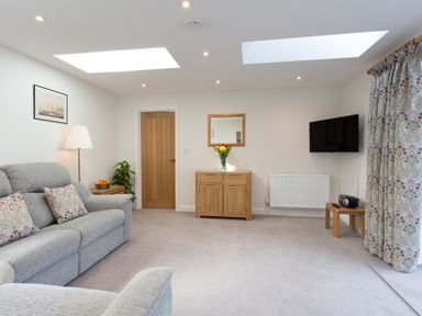 A living room with sofas a wooden cabinet and a wall mounted television at Cornish Views in Camborne